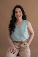 Profissional sentada no tapete, sorrindo para a câmera em ambiente claro e aconchegante.