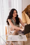 Profissional digitando no notebook; bandeja com taça e café sobre mesa de vidro.