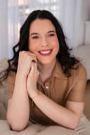 Profissional sorrindo, usando notebook perto da janela com cortinas translúcidas.